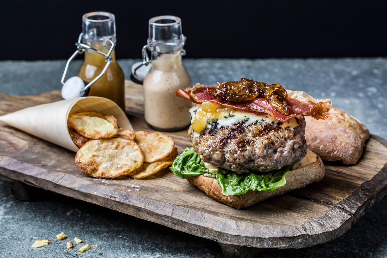 A burger with bacon and other toppings on top of a wooden board.